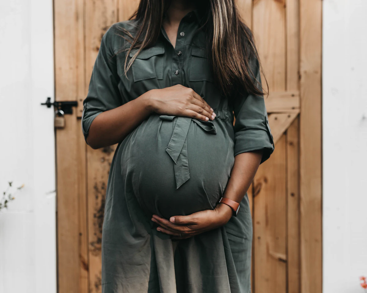 A pregnant woman in a green dress holding her belly